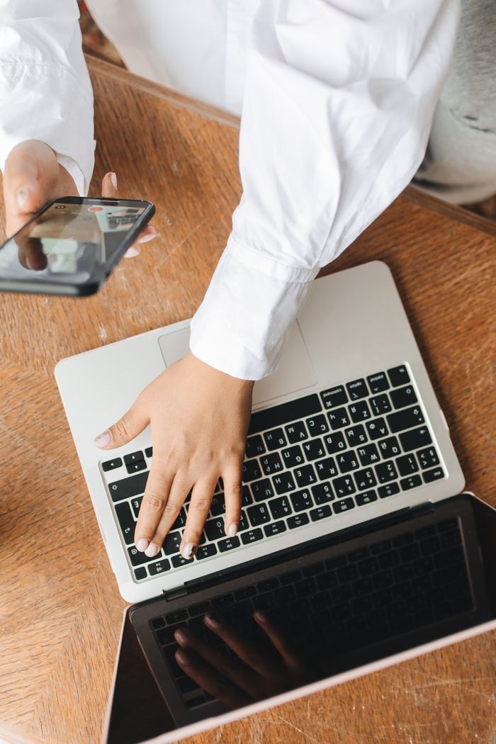 Hands working on a laptop while a smartphone is held nearby, capturing a multitasking work setting.